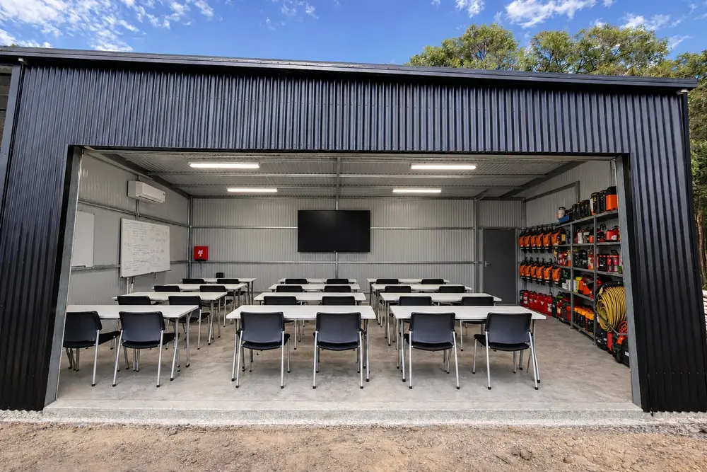 The 25-seat training room, open to the yard, with a screen and whiteboard at the far end and equipment racking along one wall.