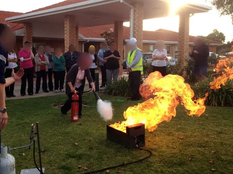Live-fire extinguisher exercise in a courtyard, a group of participants watching a burning pan.