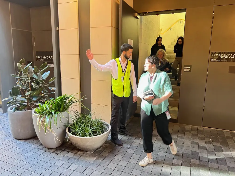 A warden in a hi-vis vest directing occupants at a building entrance during an exercise.